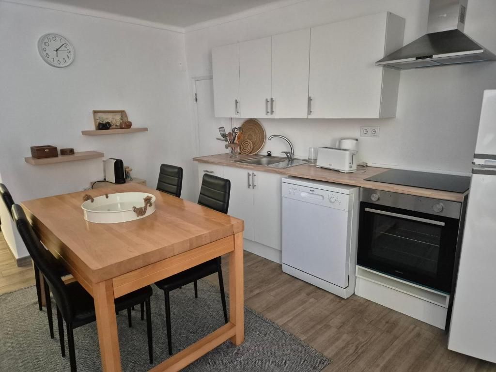 Cozinha equipada com forno, placa e máquina de lavar loiça, e mesa de jantar em madeira