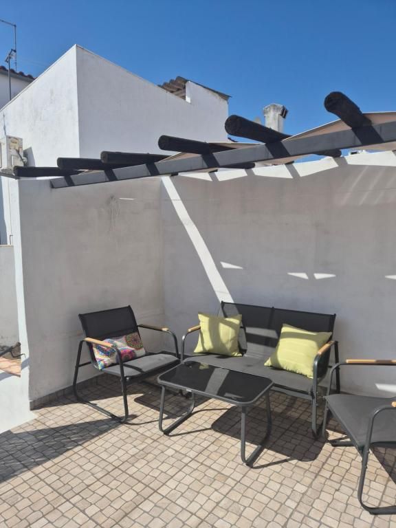 Terraço da Casa Branco com pérgola, cadeiras de exterior e almofadas amarelas, sob céu azul